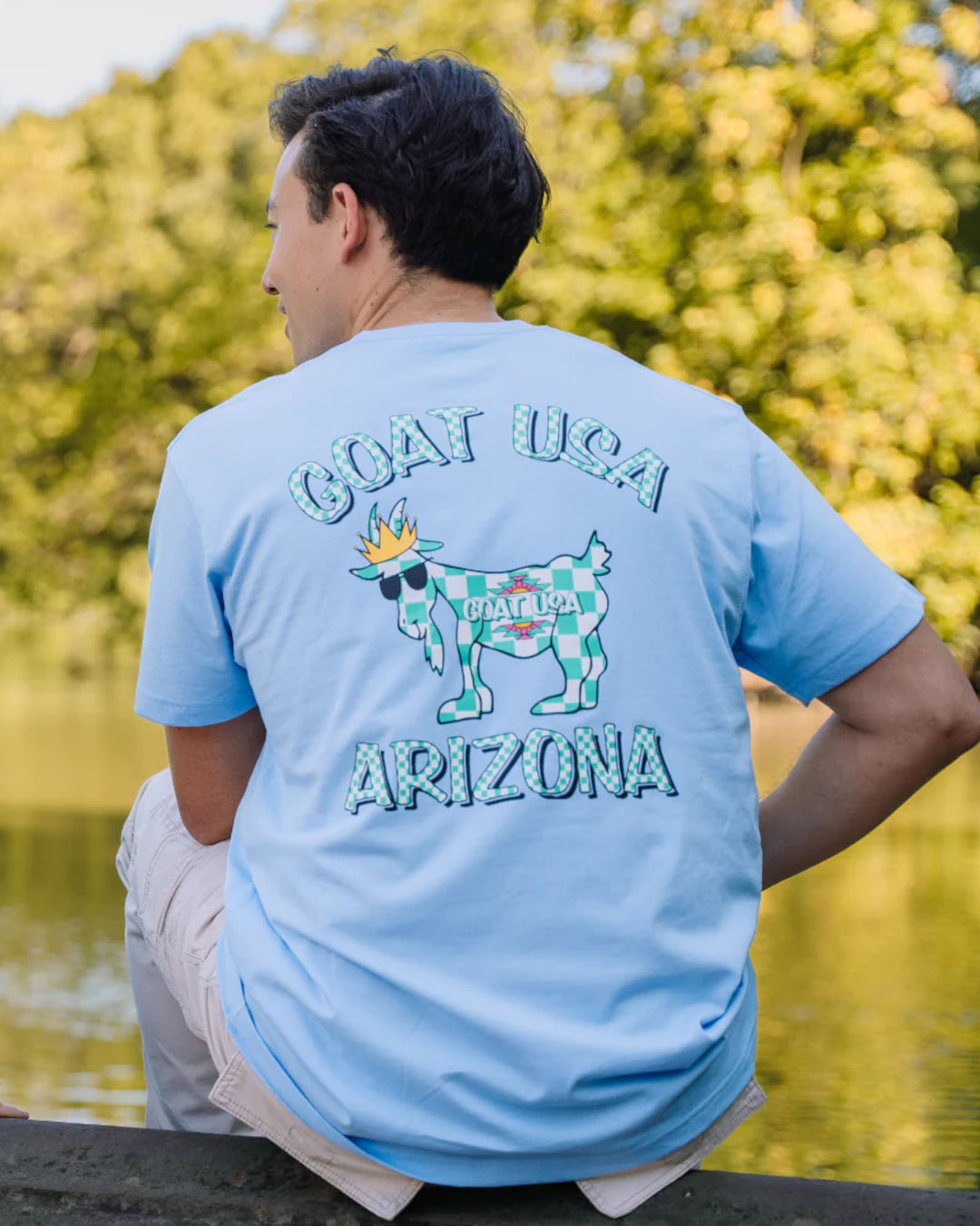 Guy sitting near pond wearing AriZona x GOAT USA t-shirt