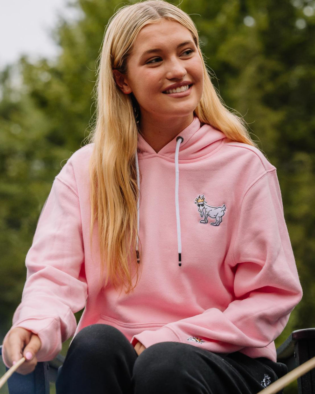 Woman sitting by campfire in pink WG Hooded Sweatshirt#color_pink