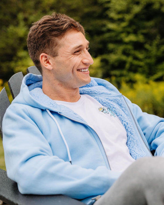 Male model sitting in lawn chair wearing Carolina Blue sherpa-lined full-zip sweatshirt#color_carolina-blue