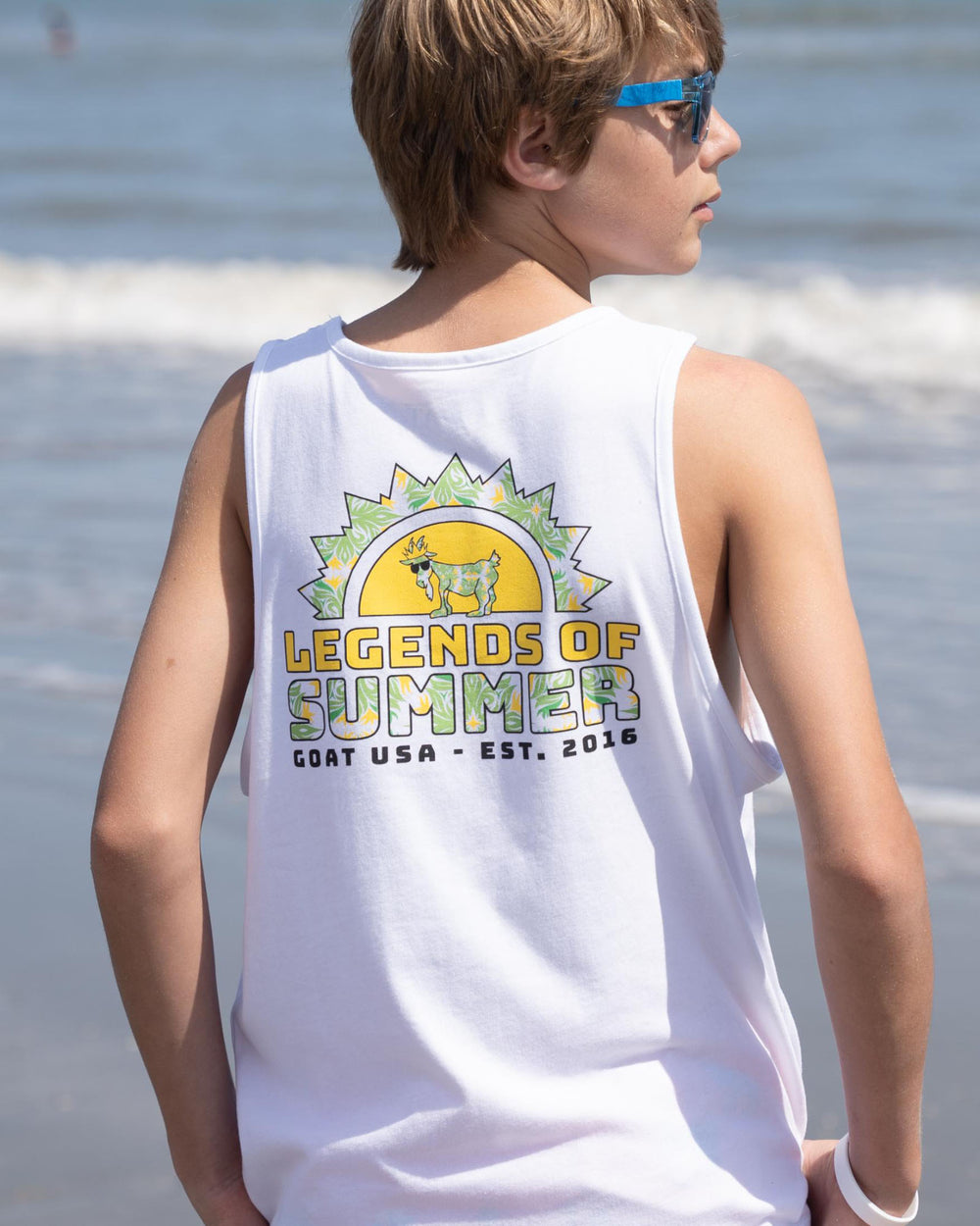 Kid wearing a white tank top on the beach looking to his side