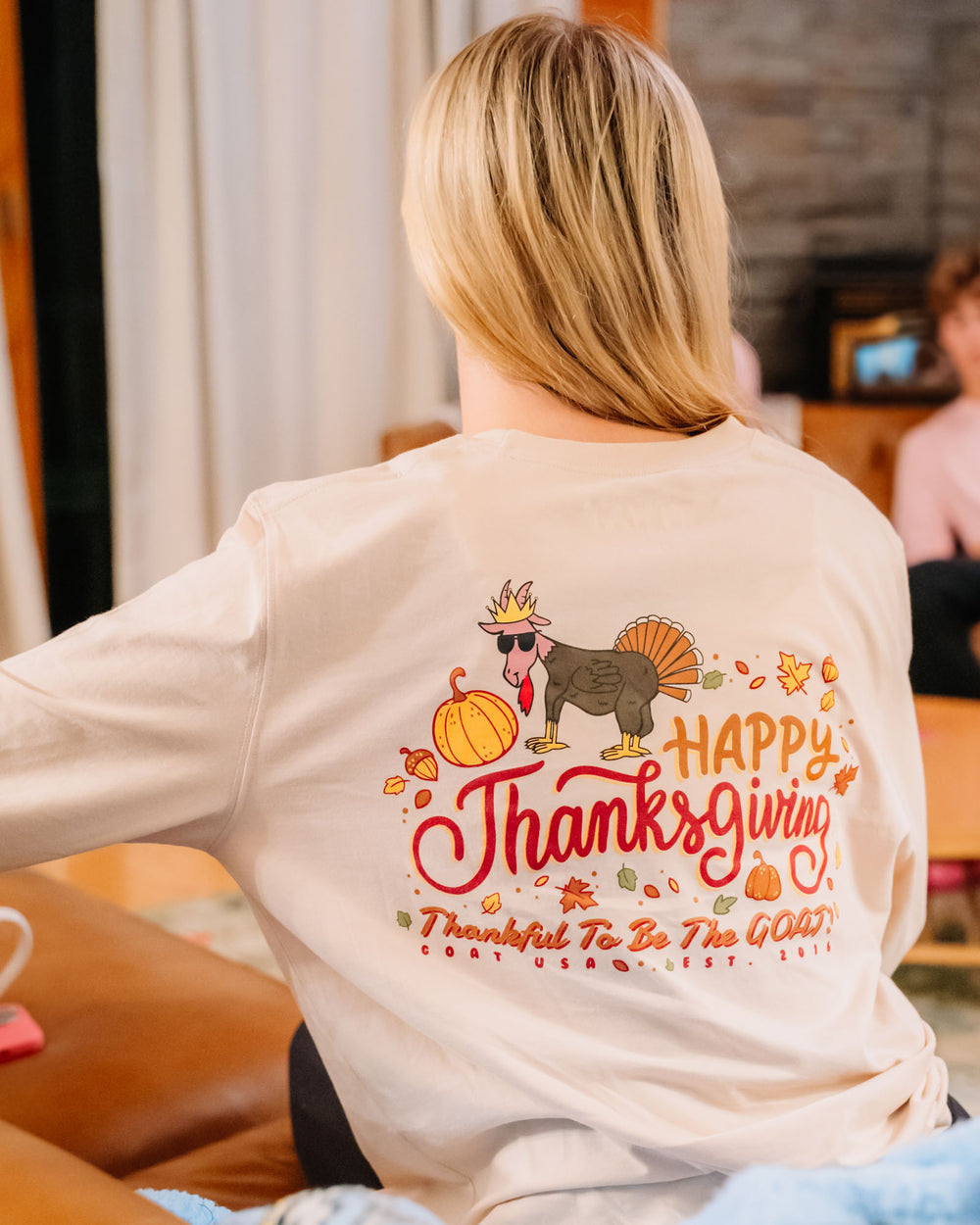 Woman sitting on couch wearing a Thanksgiving themed long sleeve