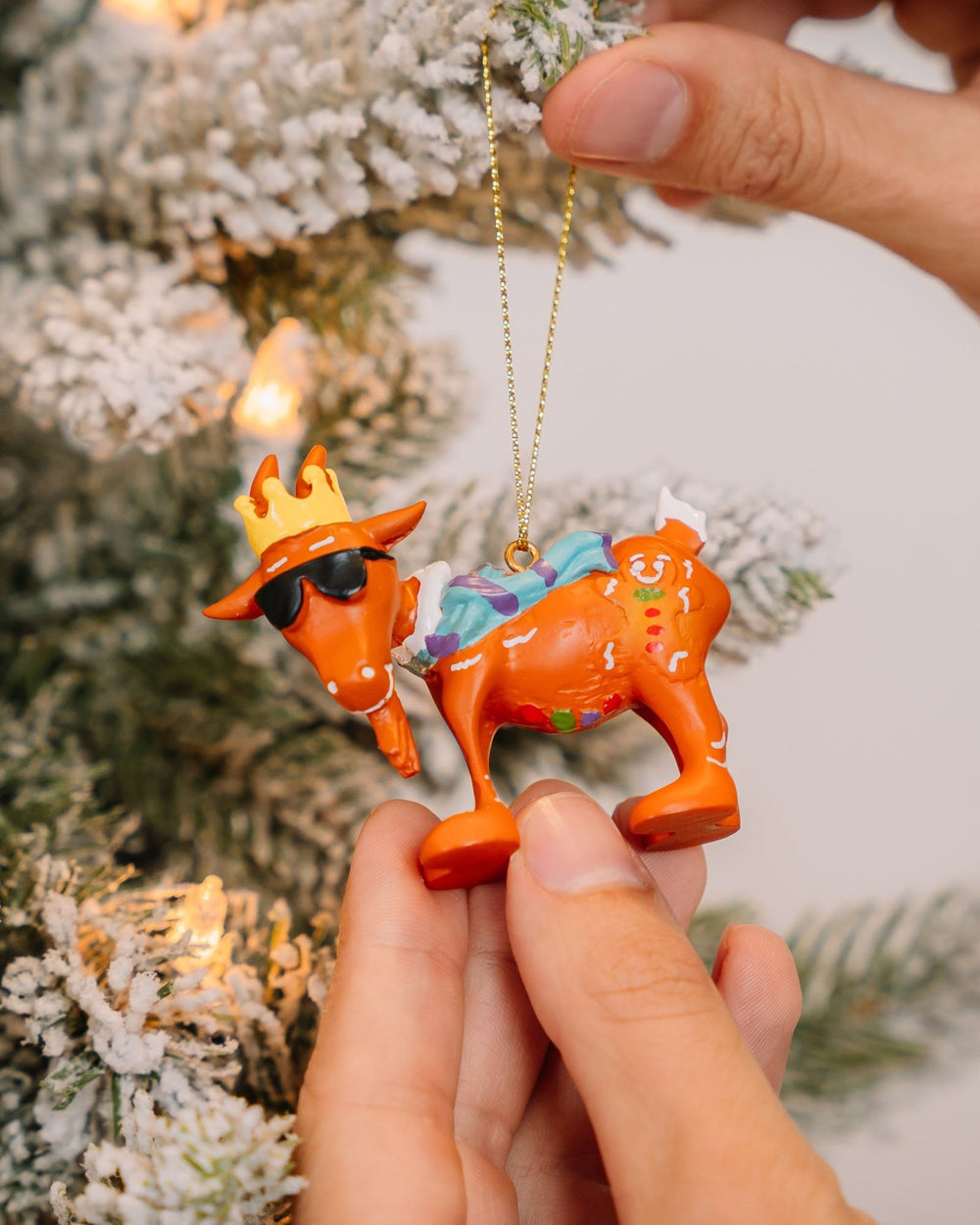 Person hanging gingerbread goat ornament on a tree